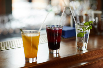 Row of three colorful drinks on bar stand, refreshing cocktails and mojito glass, copy space