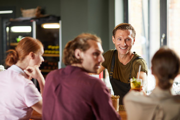 Portrait of contemporary man clinking glasses with friends while sitting at table during party and smiling happily, copy space