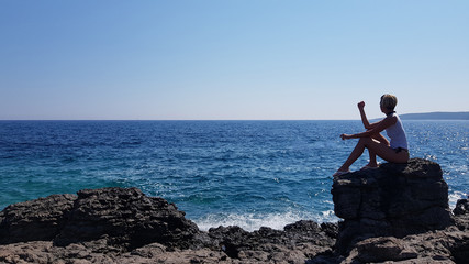 Fototapeta premium seascape and travel lifestyle, seaside a shot of the sea scenery big blue water and small woman sitting on big rock 