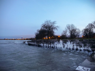 Waves crash and splash up along the corrugated steel reinforced concrete shoreline in Chicago near Foster Beach with the skyline in the distance.