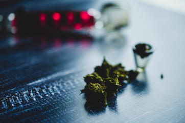Marijuana cones lie on a dark table against a glass Smoking pipe, close up. Concept of medical cannabis therapy