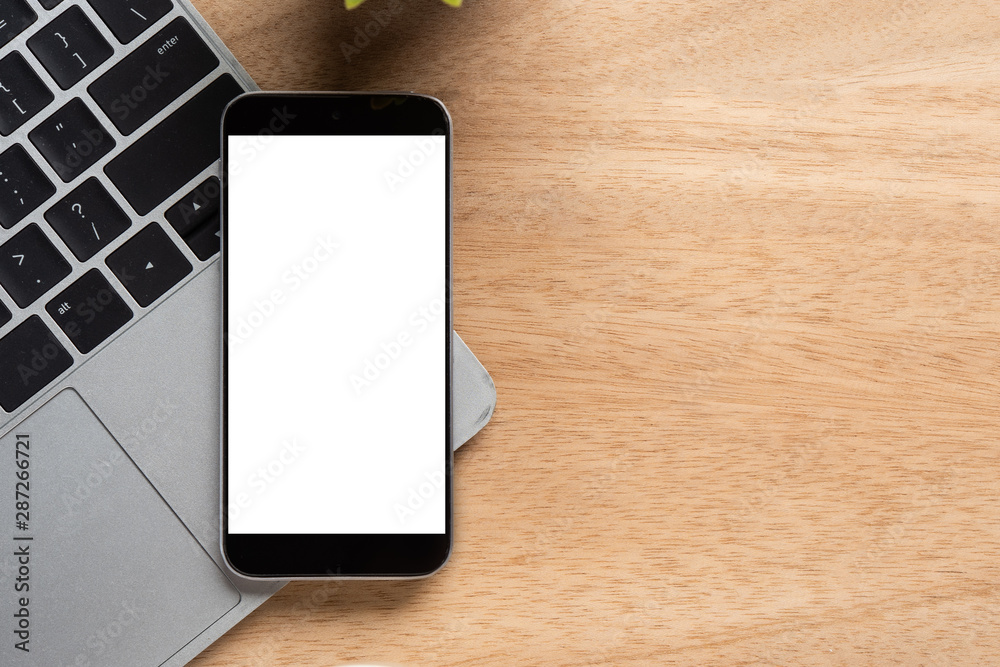 Poster smartphone with blank screen is on top of notebook over wood office desk table. top view with copy s