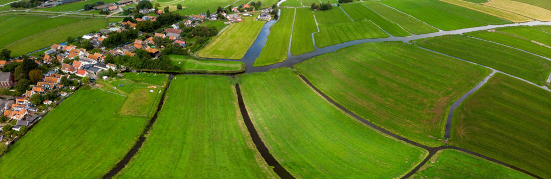Top down aerial panorama of the patterned agrarian green pasture fields with its irrigation infrastructure of ditches and trenches surrounding the small traditional village of Ransdorp near Amsterdam