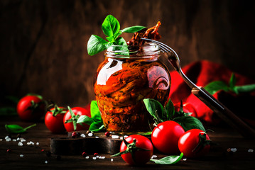 Italian Sun Dried tomatoes in olive oil with green basil and spices in glass jar on wooden kitchen table, rustic style, copy space