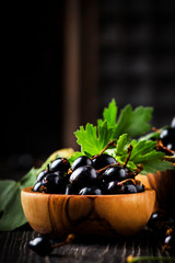 Fresh black currants in wooden bowls, on black kitchen table background, copy space, selective focus