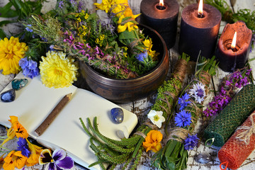 Still life with bowl of herbs, candles and old book on witch table.