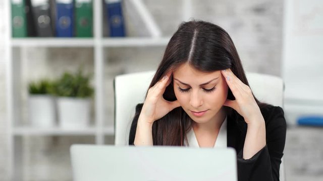 Tired young businesswoman looking at screen of laptop at office medium close-up