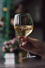 Hand sommelier holding glass of white wine. Swirling wine glass in wine tastings  White wine concept. Wine tour. Vertical, cold toning
