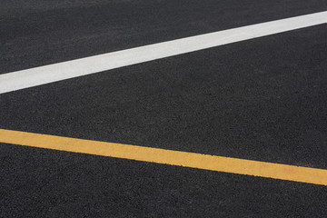 Close-up of a white paint line and a yellow paint line on a black asphalt road