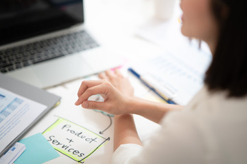 View from beside of business women working on her desk with some part of product and service planning or project proposal, focused on the woman hand in office with the meeting room atmosphere.