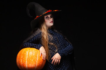 Halloween Witch with Pumpkin on black background. Beautiful young surprised woman in witches hat and costume holding pumpkin. Wide Halloween party art design. Copy-paste. Witch craft concept. Spider