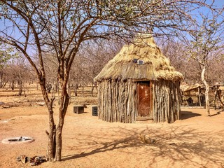 A traditional style African house in rural Namibia combined with modern technology. Walls are made of branches and mud, but small solar panels sit on its thatched roof, providing electricity.
