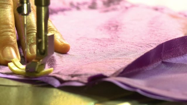 A hand held, extreme close up shot of a person sewing a purple material.