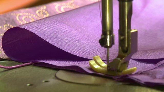 A hand held, extreme close up shot of two crafty hands sewing a tough colorful material.