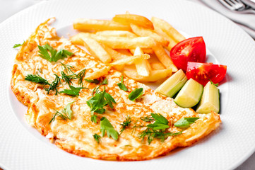 egg omelet with fried potatoes, fresh vegetables, green dill and parsley close-up on white plate 