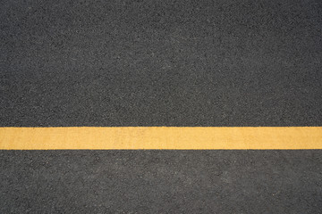Fototapeta premium A parallel yellow paint line close-up text space on black asphalt road