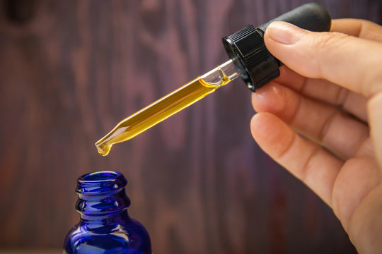 CBD (Cannabidiol) oil dosage measured out of blue bottle with dropper. on wooden background