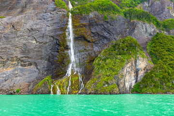The turquoise fjord of the Last Hope with a waterfall along a cliff near the Torres del Paine...