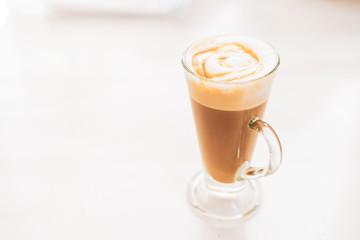 Hot caramel macchiato in a tall glass with caramel sauce on top close up.
