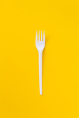 One white plasti fork on saturated yellow background as a symbol of consumption. Eco and fast food concept.