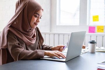 Arab businesswoman brown hijab shop online with a purple credit card on mockup white screen laptop at home.