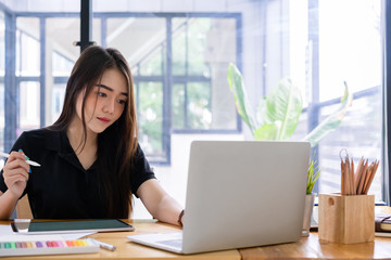 Beautiful young asian freelance graphic designer hand working with stylus pen and laptop computer...