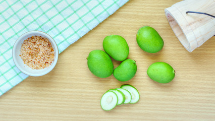 Fototapeta na wymiar Close-up group of raw green mango and slices mango on wooden table background. With a wooden bucket and clean green and white checkered pattern hand towel placed on a wooden table.