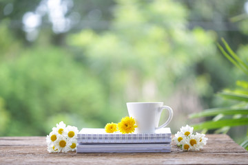 Obraz na płótnie Canvas White coffee cup with Chrysanthemum flowers and notebooks on wooden table at outdoor