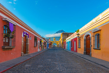Cityscape of the colorful main street of Antigua city at sunrise with the famous yellow arch and the Agua volcano in the background, Guatemala, Central America.