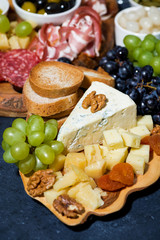 cheese platter on a wooden board, bread and fruit, vertical top view