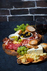cheese platter, bread, fruit and cold cuts to wine on dark background