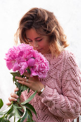 Fototapeta premium Portrait of a beautiful young Caucasian woman 20 years old model in brown knit sweater with natural make-up and pink flower peonies posing on white isolated background