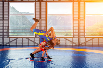 A little wrestler boy in a sports tights wrestles with an adult male wrestler on a wrestling carpet...