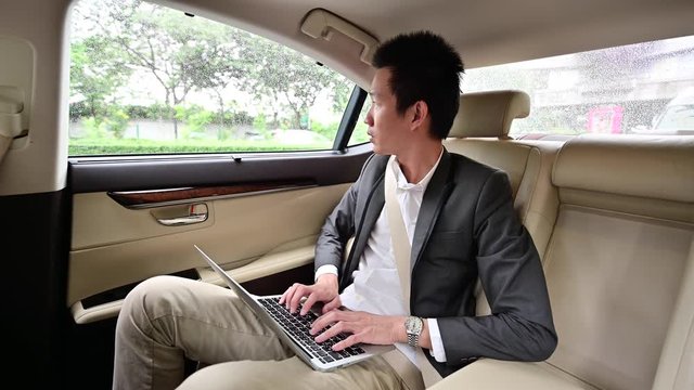 4K Young businessman using laptop on the backseat of a car