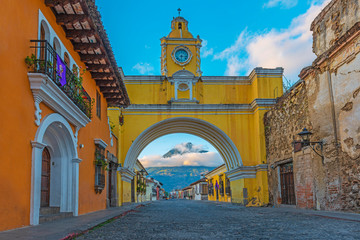 The colorful yellow arch of Antigua city at sunrise with the active Agua volcano in the background,...