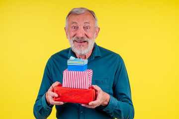 portrait amazed caucasian old elderly man holding two boxex of gifts in studio yellow background