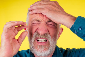 Senior older man holding a pain relief tablet or pill memory loss studio yellow background . heart...