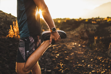 Male runner stretching leg and feet and preparing for running outdoors. Smartwatches or fitness tracker on hand. Beautiful sun light on background. Active and healthy lifestyle concept.