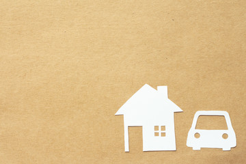 White paper cut of home and car with copy space on brown background.