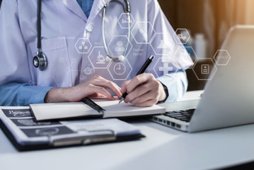 Young female in uniform of doctor using digital technology laptop for Output Device and writing a patient report on the office desk.