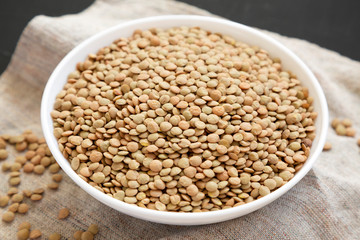 Organic green lentils in a white bowl on a black background, side view. Close-up.