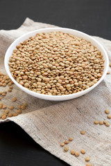 Organic green lentils in a white bowl on a black background, side view. Close-up.