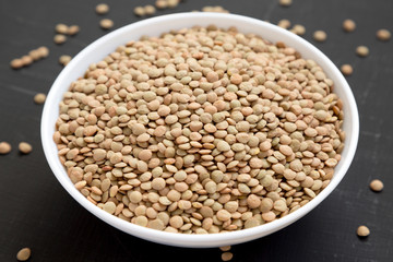 Organic green lentils in a white bowl on a black surface, side view. Close-up.