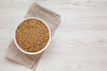 Organic green lentils in a white bowl on a white wooden background, top view. Flat lay, overhead, from above. Copy space.