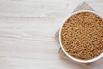 Organic green lentils in a white bowl on a white wooden surface, top view. Copy space.