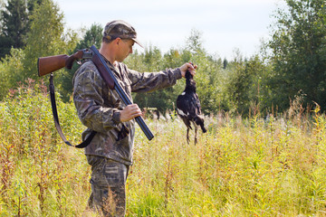 hunter with a shotgun holding a downed grouse