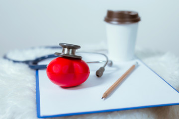 Medical stethoscope and a red heart and a coffee cup placed on a document on a white background. The concept of treating heart disease.