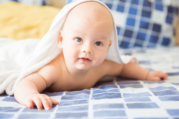 Cute baby under the towel after bathing on blue plaid bed