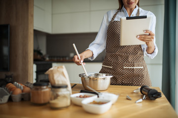 Young woman using tablet in kitchen where read cake recipe