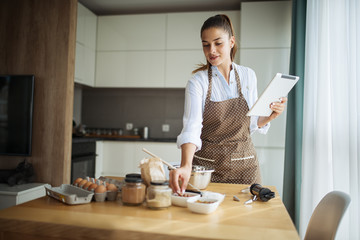 Young woman using tablet in kitchen where read cake recipe